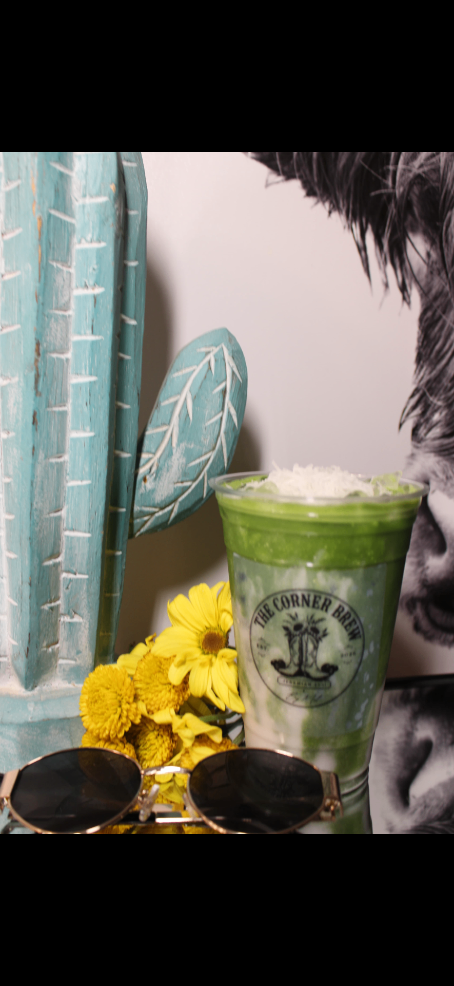 Iced coconut matcha latte topped with shredded coconut, styled with a wooden cactus