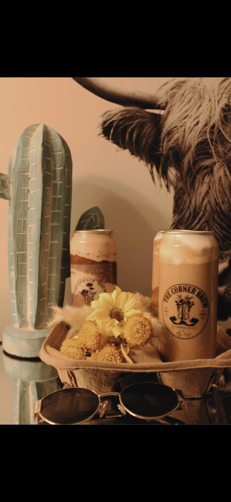 Two Corner Brew sealed latte cans nestled with sunflowers and a wooden cactus